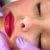 Professional Beautician applying permanent red color make up on lips with tattoo tool and purple medical gloves in beauty studio. Close up. Make up concept. Top view.