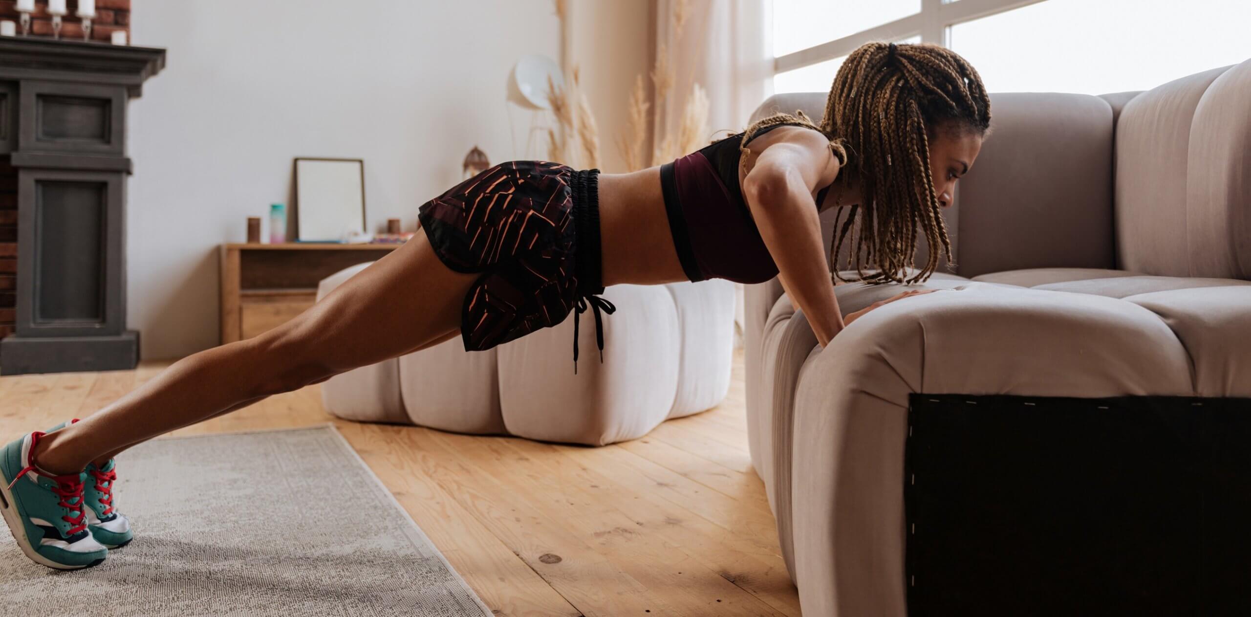 Woman wearing shorts and top doing pushups near sofa
